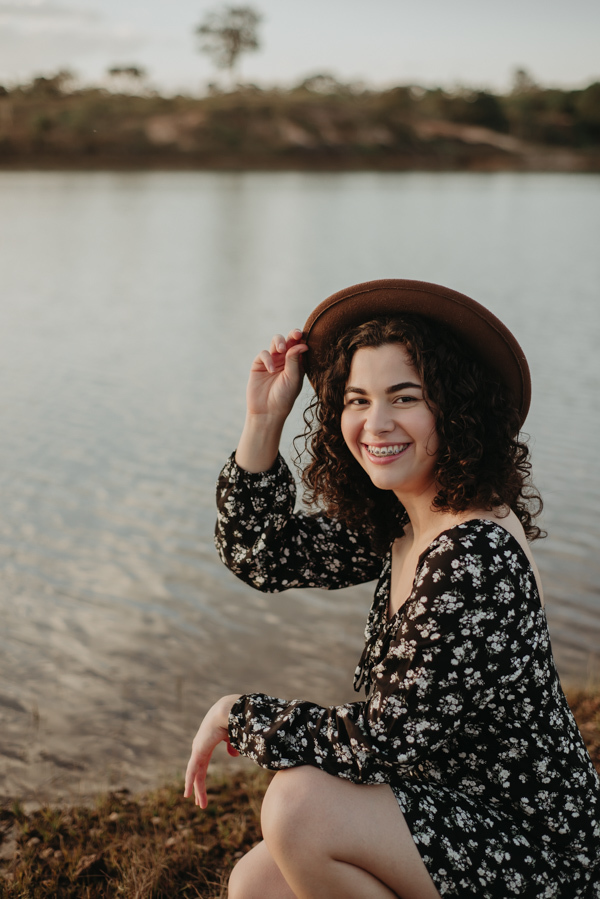 ensaio feminino externo a beira do lago com roupa preta e branca e chapeu marron estilo boho, menina cacheada