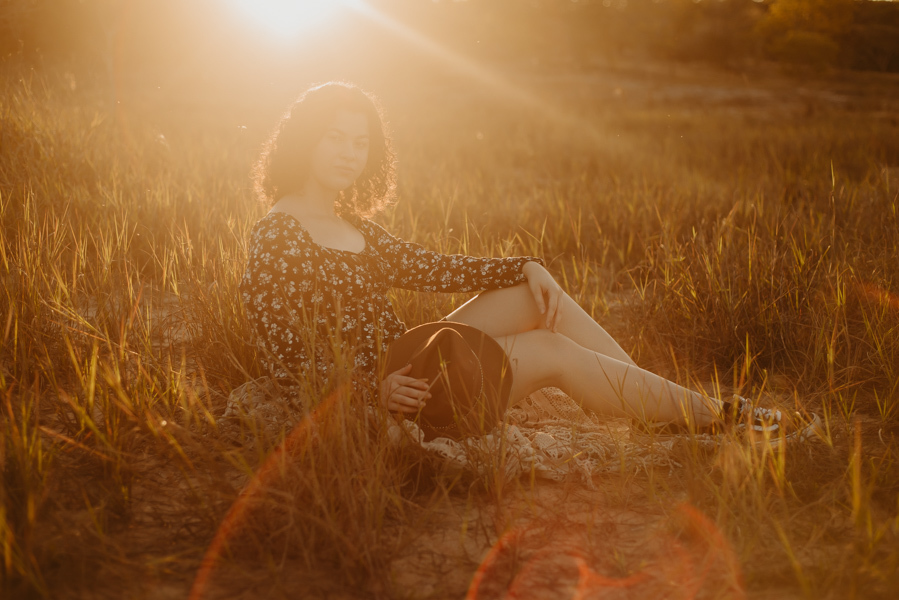 ensaio feminino externo a beira do lago com roupa preta e branca e chapeu marron estilo boho, menina cacheada. fotos no por do sol, 