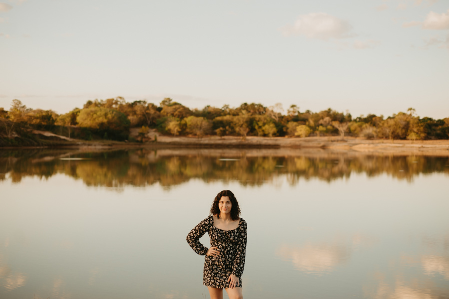ensaio feminino externo a beira do lago com roupa preta e branca e chapeu marron estilo boho, menina cacheada. fotos no por do sol, 