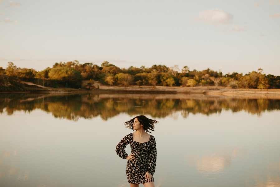 ensaio feminino externo a beira do lago com roupa preta e branca e chapeu marron estilo boho, menina cacheada. fotos no por do sol, 