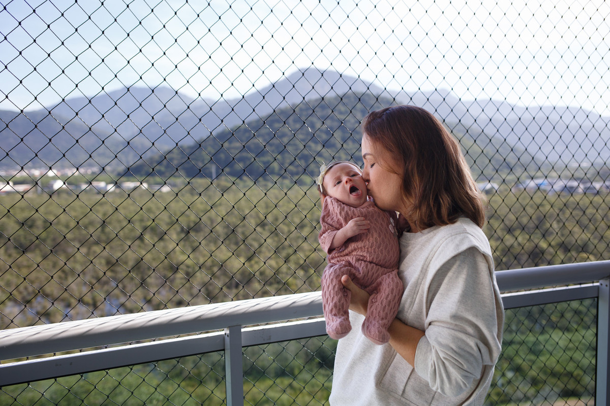 foto da mãe com bebê no colo em varanda com fundo verde