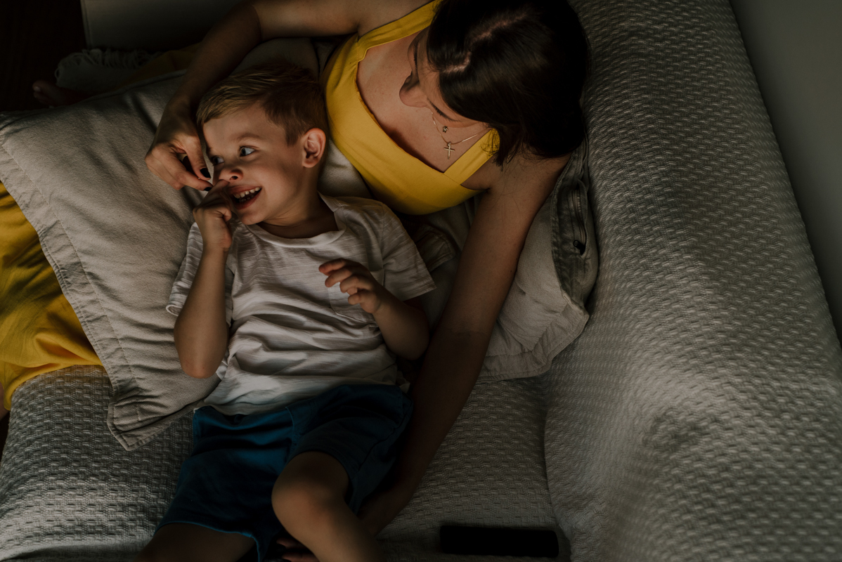 Garoto abraçado à mãe no sofá, transmitindo segurança e amor incondicional, um registro de carinho entre mãe e filho.
