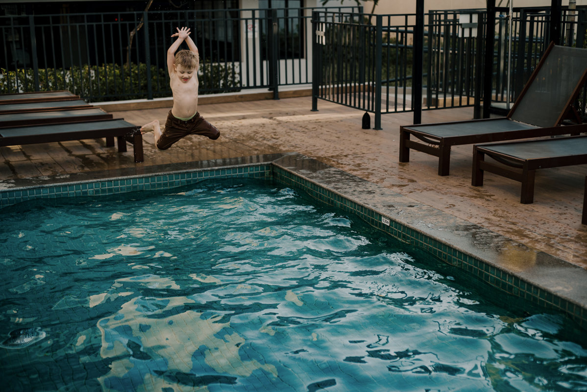 Criança se divertindo na piscina, sorrindo e aproveitando a infância, com a água e a luz natural criando um cenário perfeito.