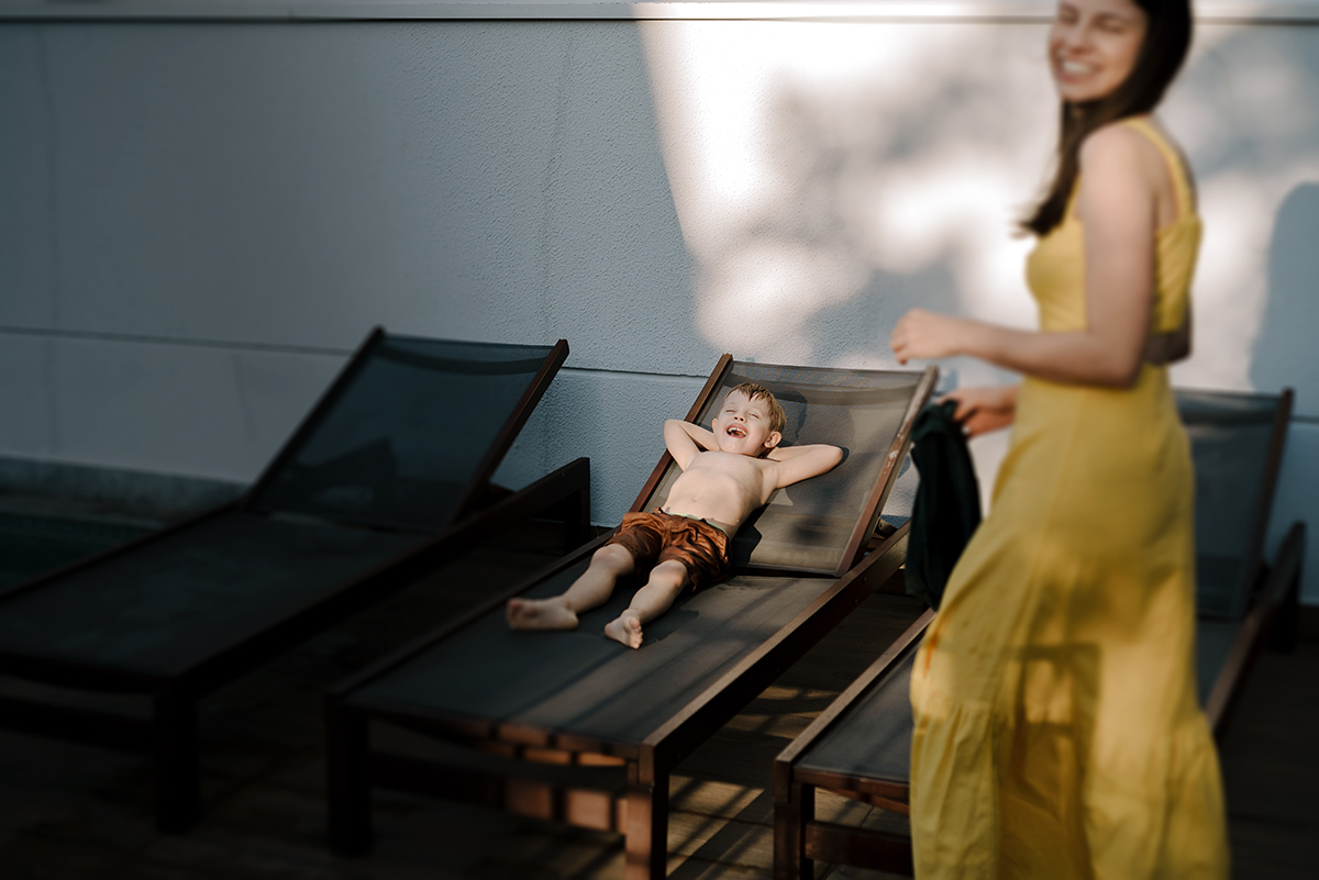 Mãe de vestido amarelo, segurando a mão do filho enquanto caminham juntos, capturando a cumplicidade e o afeto entre ambos.
