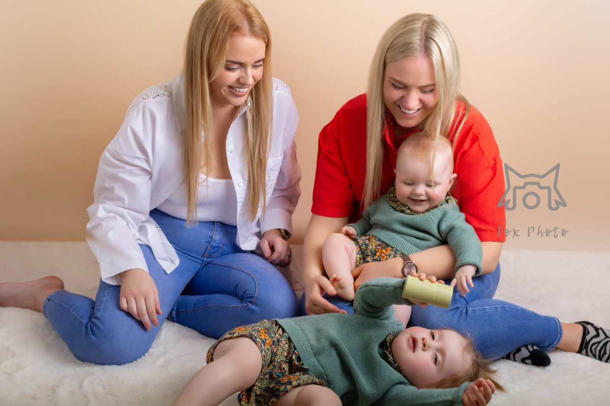 two mother onde holding a baby other looking at the daught playing all laoughinf 