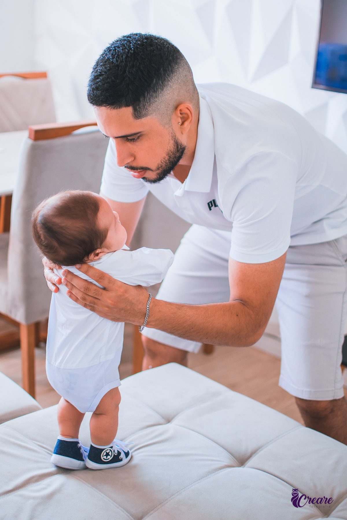 Ensaio newborn lifestyle, ensaio família. A imagem contém: um homem jovem com roupa branca, uma mulher jovem com roupa branca, um bebê com roupa branca e bermuda bege com suspensório. fotógrafo Mauá, ensaio lifestyle. 