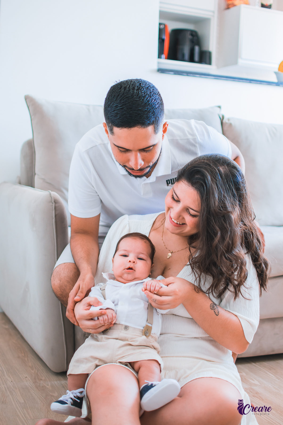Ensaio newborn lifestyle, ensaio família. A imagem contém: um homem jovem com roupa branca, uma mulher jovem com roupa branca, um bebê com roupa branca e bermuda bege com suspensório. fotógrafo Mauá, ensaio lifestyle. 
