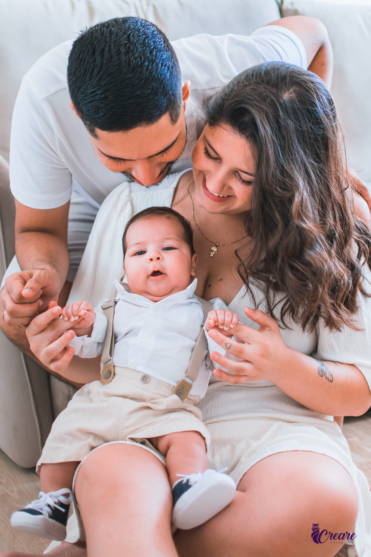 Ensaio newborn lifestyle, ensaio família. A imagem contém: um homem jovem com roupa branca, uma mulher jovem com roupa branca, um bebê com roupa branca e bermuda bege com suspensório. fotógrafo Mauá, ensaio lifestyle. 