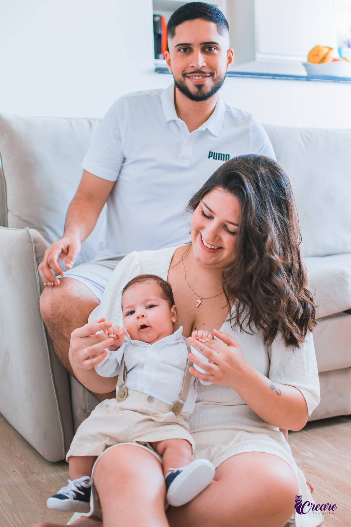 Ensaio newborn lifestyle, ensaio família. A imagem contém: um homem jovem com roupa branca, uma mulher jovem com roupa branca, um bebê com roupa branca e bermuda bege com suspensório. fotógrafo Mauá, ensaio lifestyle. 