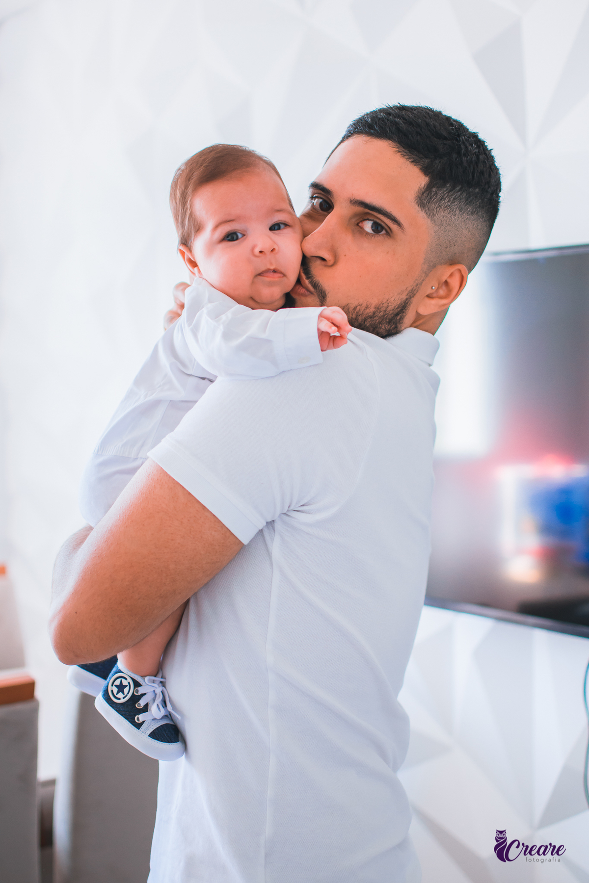 Ensaio newborn lifestyle, ensaio família. A imagem contém: um homem jovem com roupa branca, uma mulher jovem com roupa branca, um bebê com roupa branca e bermuda bege com suspensório. fotógrafo Mauá, ensaio lifestyle. 