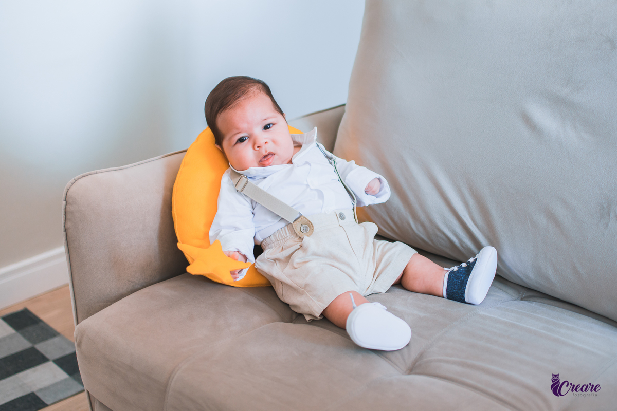 Ensaio newborn lifestyle, ensaio família. A imagem contém: um homem jovem com roupa branca, uma mulher jovem com roupa branca, um bebê com roupa branca e bermuda bege com suspensório. fotógrafo Mauá, ensaio lifestyle. 