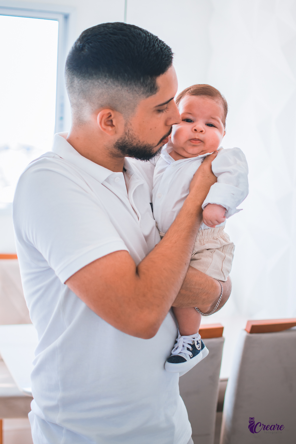 Ensaio newborn lifestyle, ensaio família. A imagem contém: um homem jovem com roupa branca, uma mulher jovem com roupa branca, um bebê com roupa branca e bermuda bege com suspensório. fotógrafo Mauá, ensaio lifestyle. 