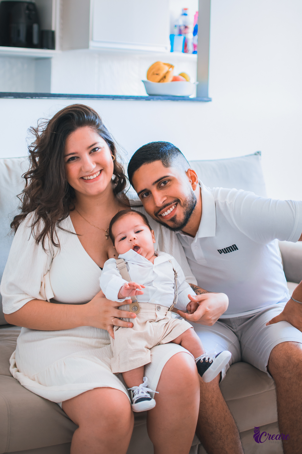 Ensaio newborn lifestyle, ensaio família. A imagem contém: um homem jovem com roupa branca, uma mulher jovem com roupa branca, um bebê com roupa branca e bermuda bege com suspensório. fotógrafo Mauá, ensaio lifestyle. 