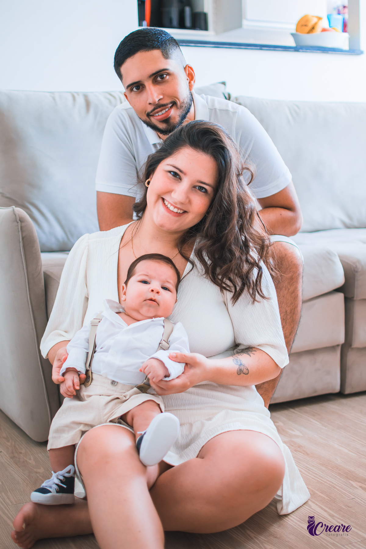 Ensaio newborn lifestyle, ensaio família. A imagem contém: um homem jovem com roupa branca, uma mulher jovem com roupa branca, um bebê com roupa branca e bermuda bege com suspensório. fotógrafo Mauá, ensaio lifestyle. 