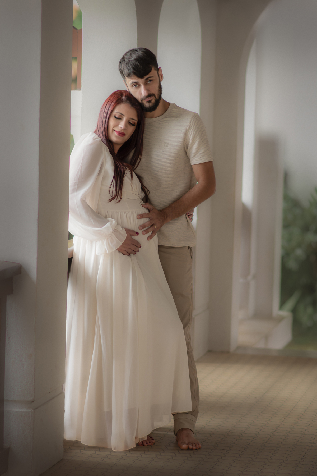 Ensaio fotográfico de gestante que o casal está abraçado acariciando a barriga da mulher grávida.