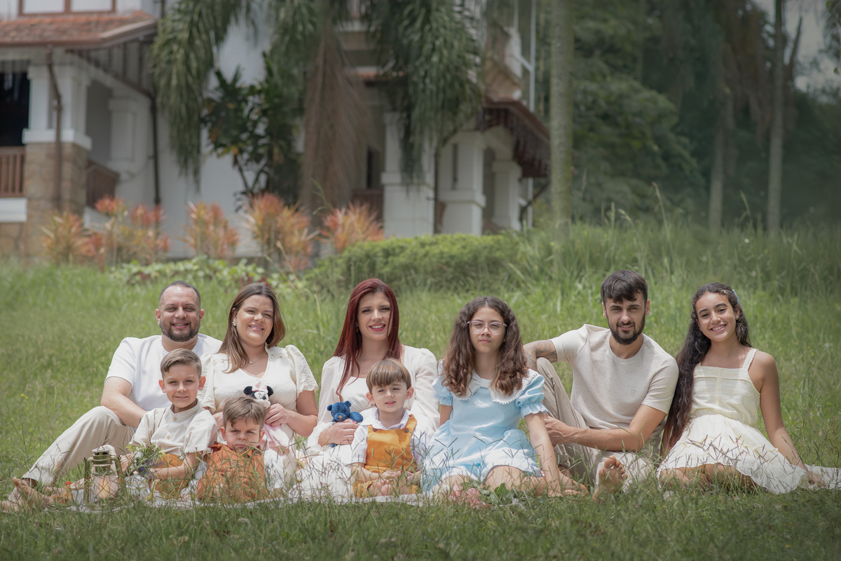 grupo de pessoas sentados na grama todos olhando para frente em direção a camera, ao fundo uma casa grande.