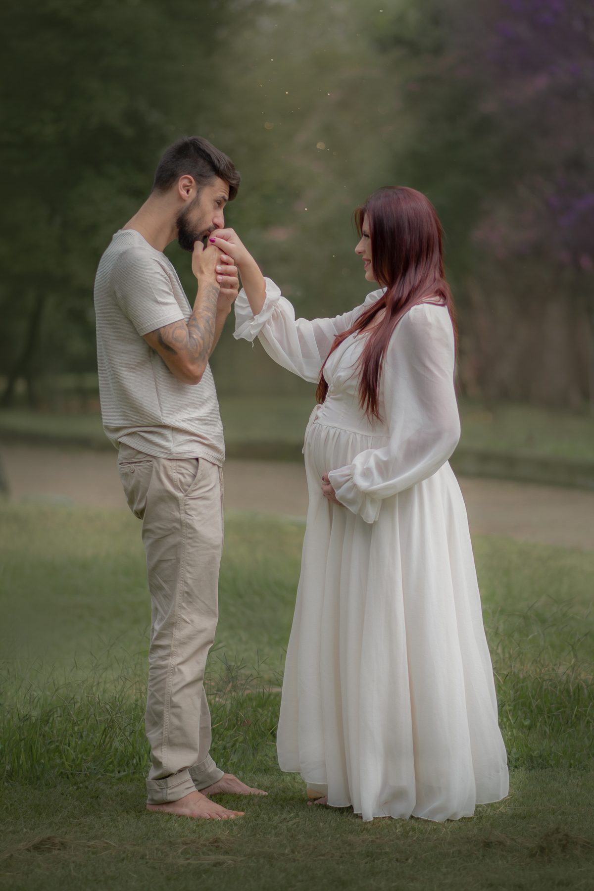 Um casal em pé de frente um para o outro, o homem beija a mãr da mulher grávida durante um ensaio fotográfico no Parque Chácara Silvestre em Sâo Bernardo do Campo.