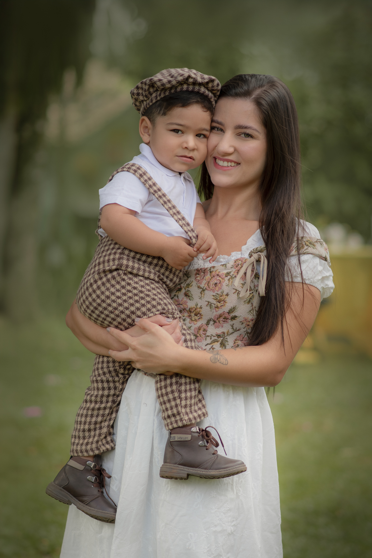 Uma mulher comseu filho no colo, os dois usam roupas bucólicas, durante o ensaio de dia das mães ao ar livre.