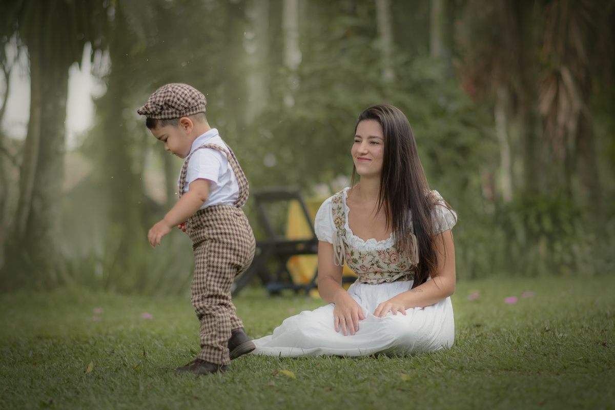 Uma mulher observando seu filho pequeno brincar na grama, durante o ensaio fotográfico de dia das mães.