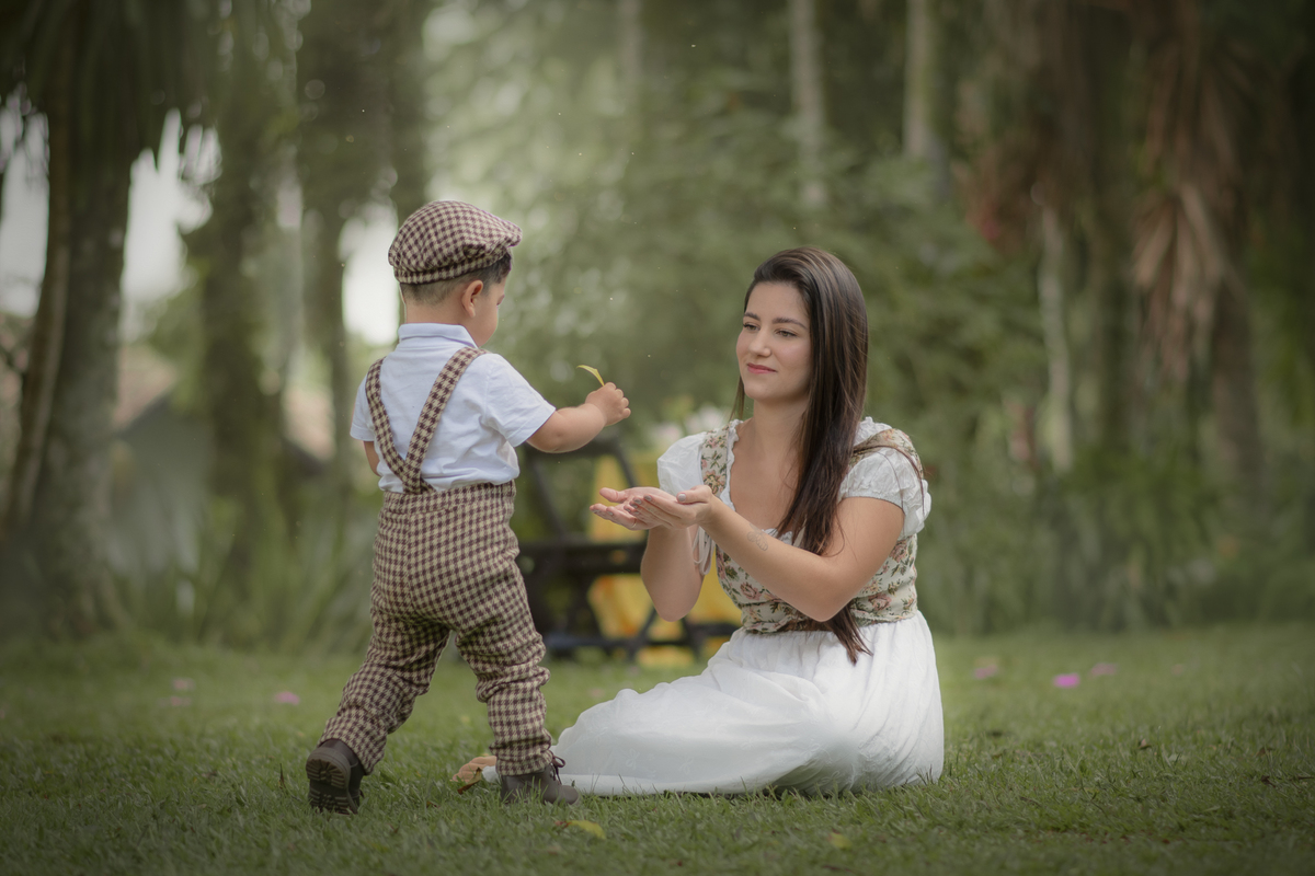 Uma mulher brincando na grama com seu filho pequeno, durante o ensaio fotográfico de dia das mães.