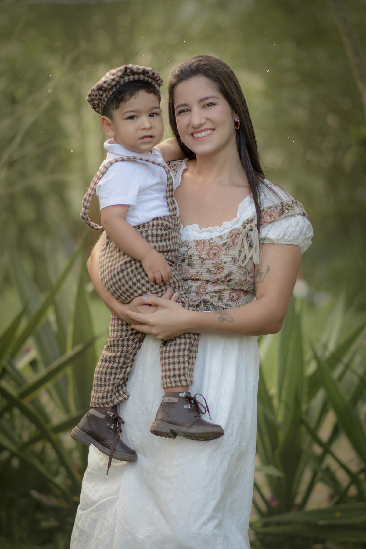Uma mulher comseu filho no colo, os dois usam roupas bucólicas, durante o ensaio de dia das mães ao ar livre.