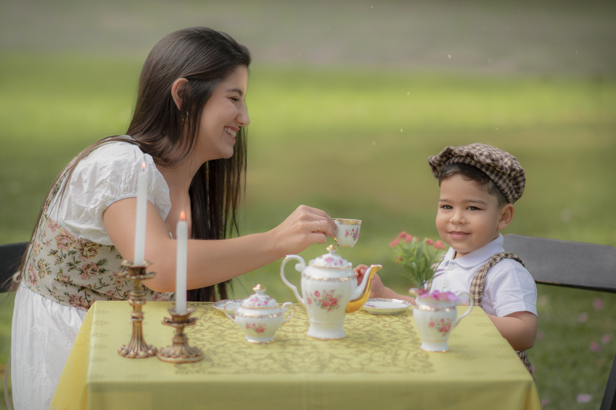 Uma mãe e seu filho em Uma mesa com toalha amarela com aparelhos de chá com dois castiçais com velas.