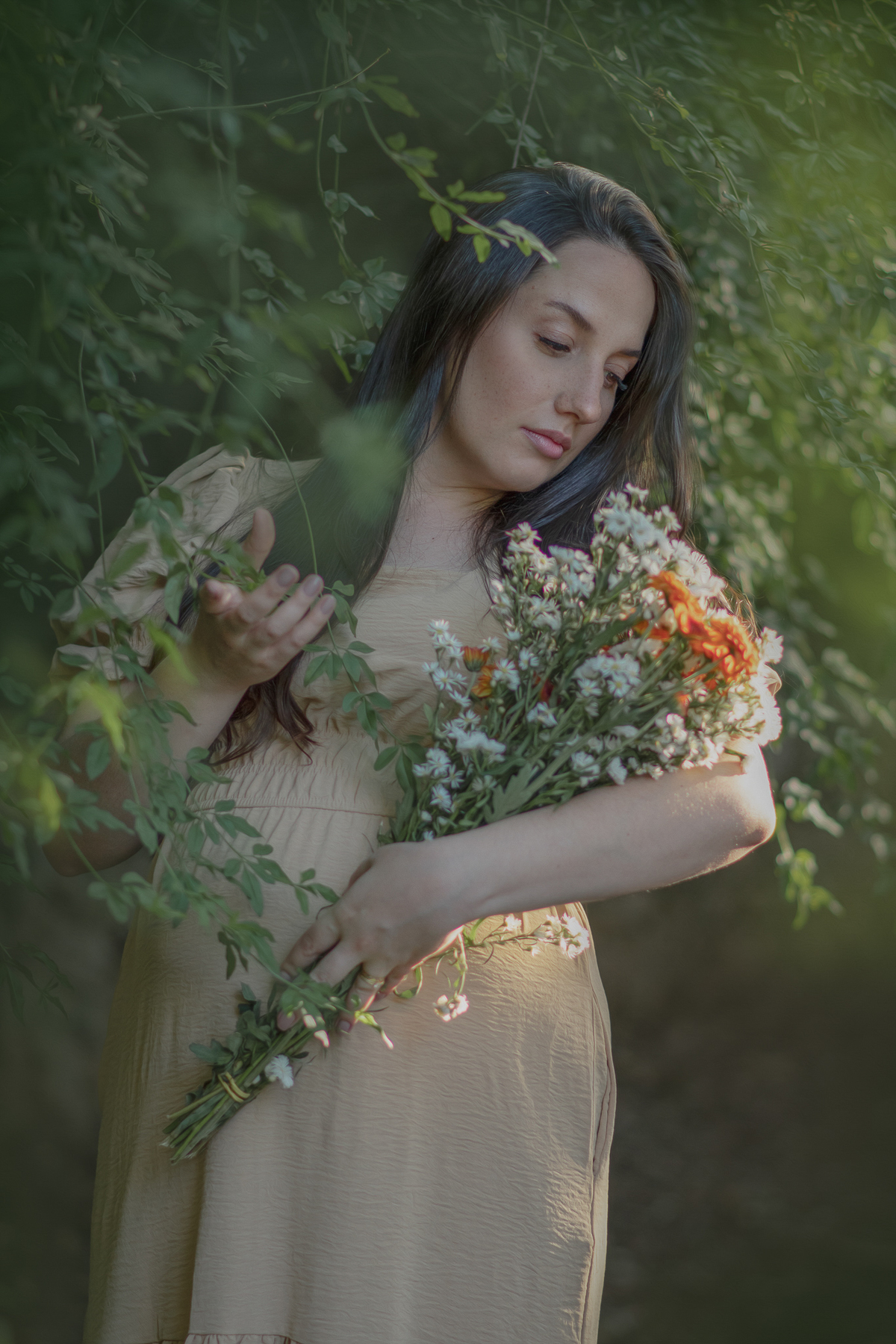 uma mulher sentada ao chão de um parque com muito verde em volta, durante um ensaio fotográfico de gestante e a sua frente tem uma cesta com flores.