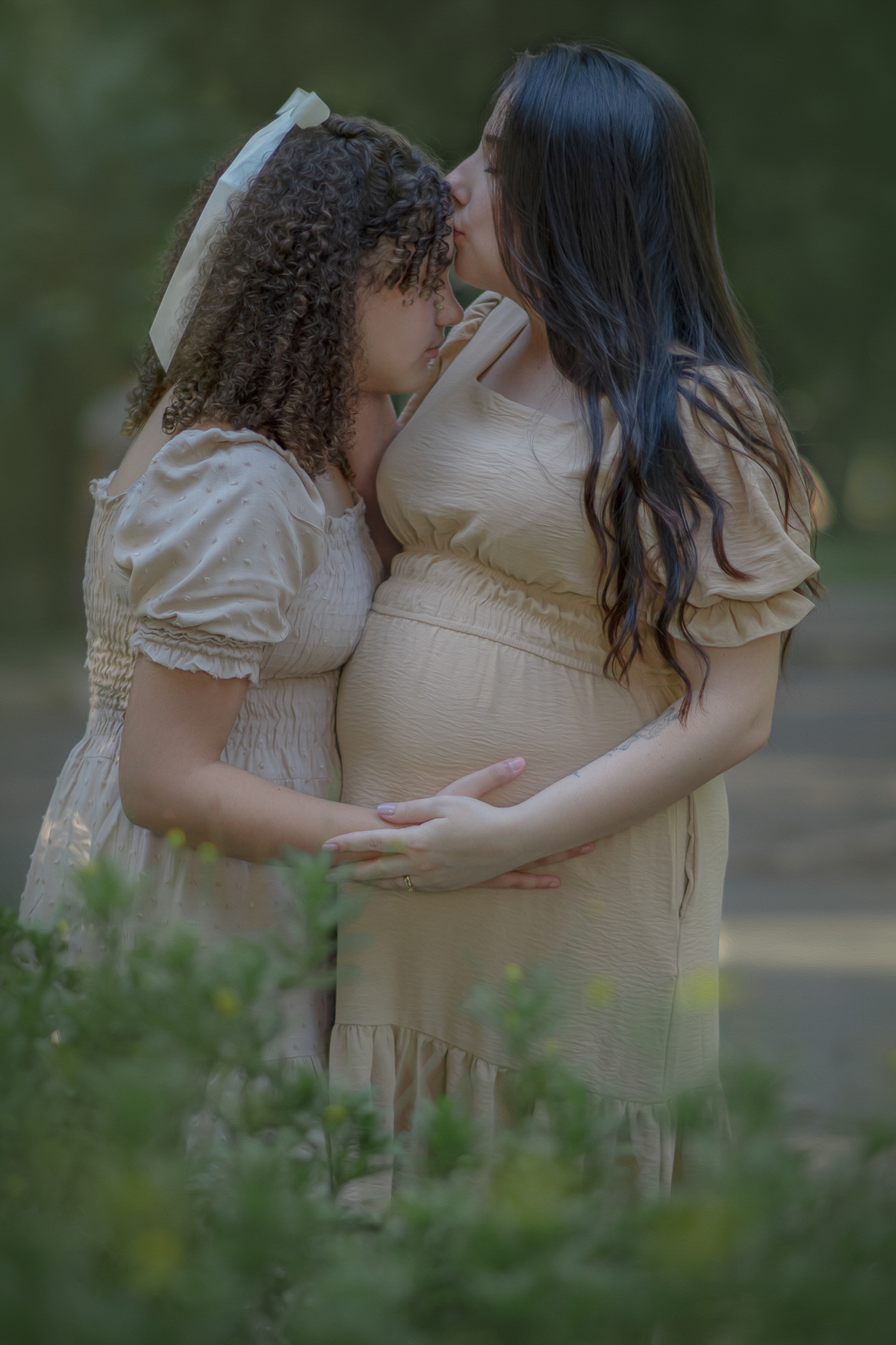 Uma mulher gestante beijando a testa de sua filha adolescente, durante o ensaio fotográfico no Parque Chico mendes.