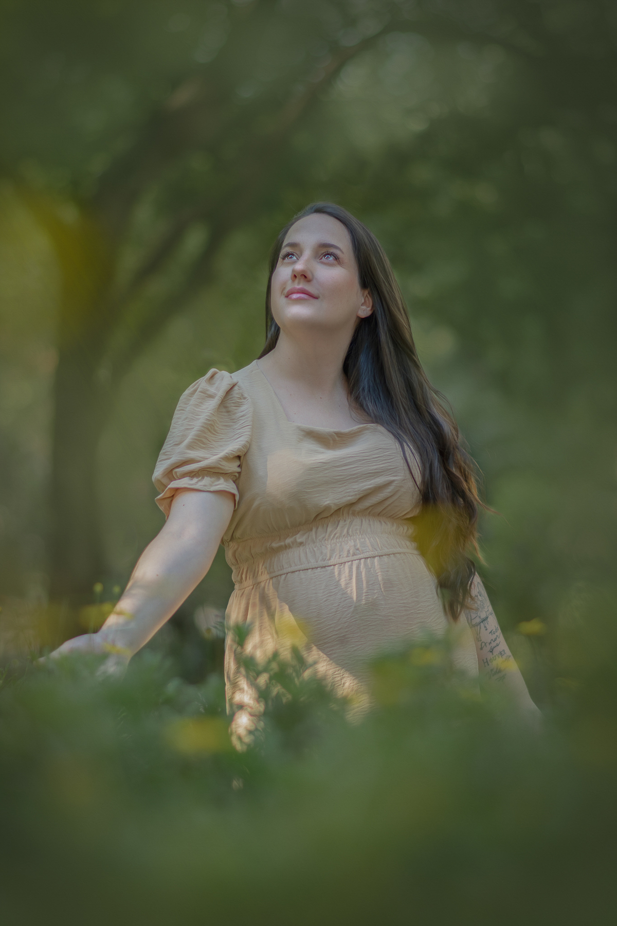 Uma mulher em um parque durante ensaio gestante, ela toca das flores amarelas e olha o sol bater em seu rosto.