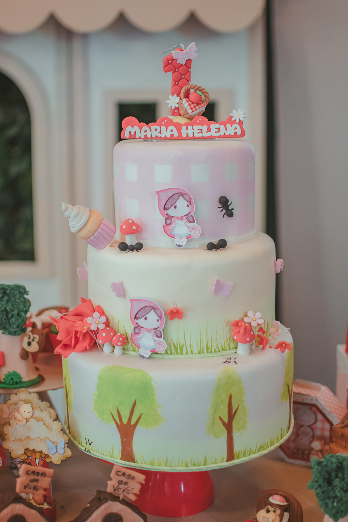 Bolo de aniversário de 1 ano decorado com tema de chápeuzinho vermelho e uma vela em cima com número 1 e o nome Maria Helena.