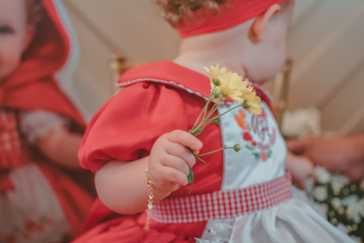 detalhes da mão de uma bebê de um ano segurando uma flor amarela durante a sua festa de aniversário.
