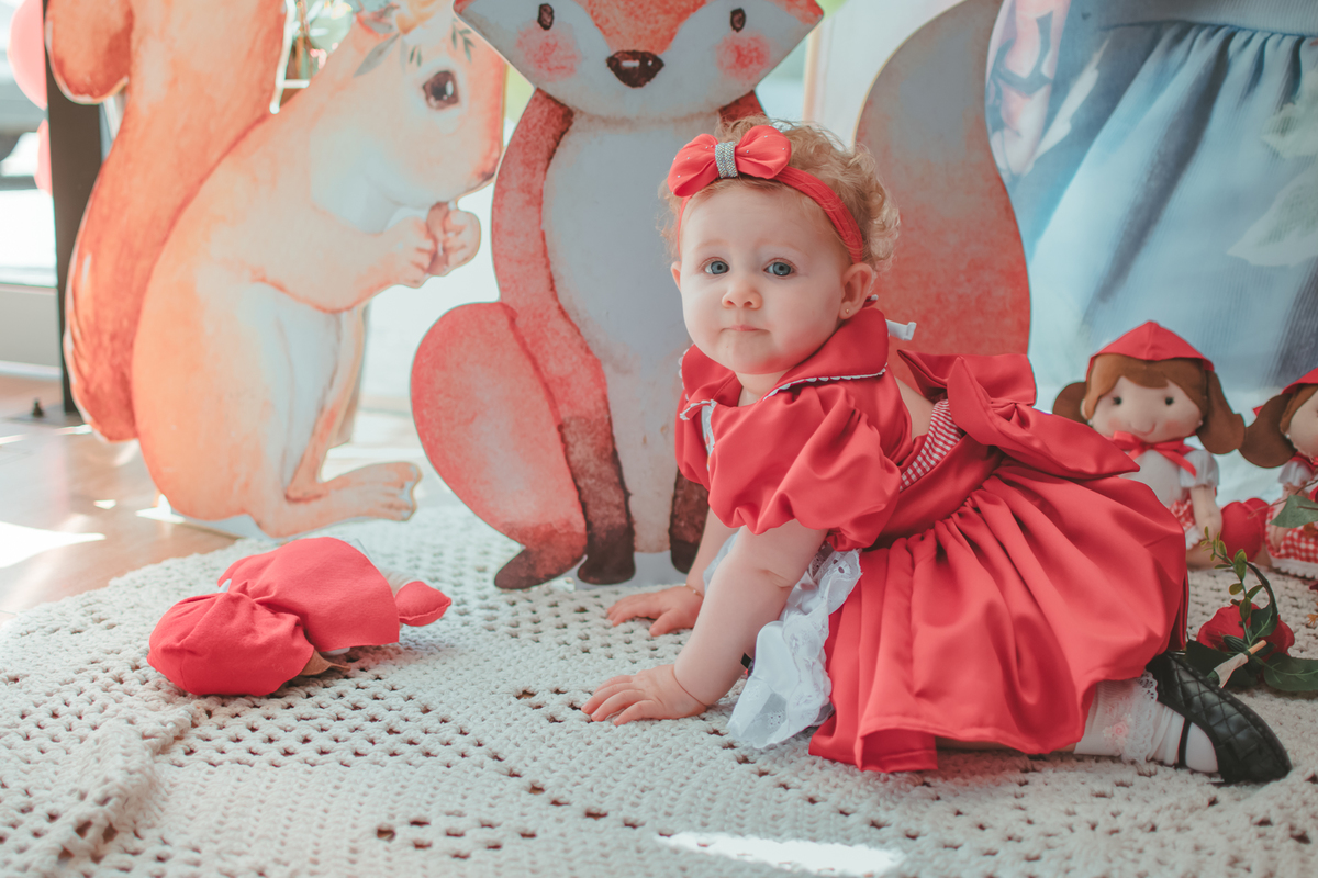 Bebê de uma no engatinhando no chão em frente um decoração de festa de aniversário com tema Chapeuzinho Vermelho.