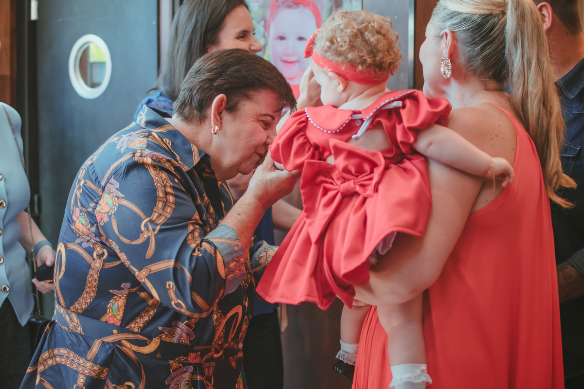 Uma mulher de idade, beijando a mão de uma bebê durante a festa de aniversário de um ano dela. 