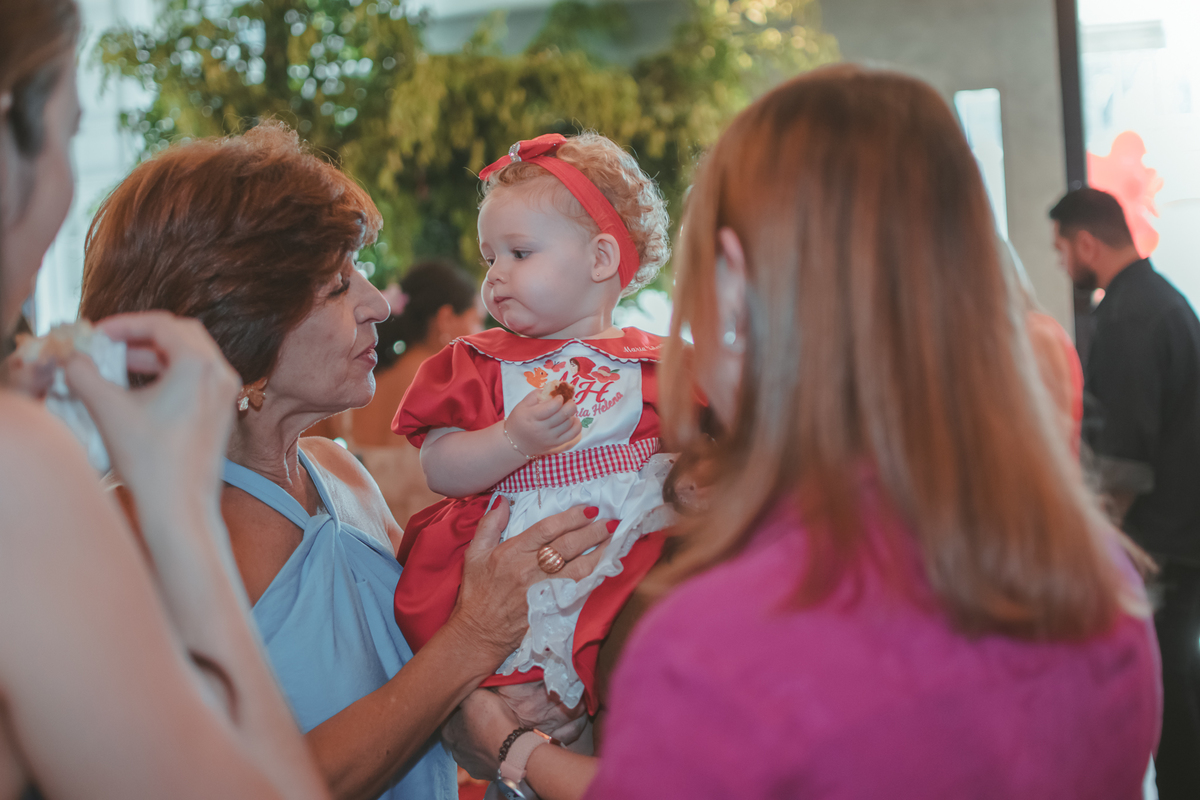 Um senhora de idade olhando para a bebê, que retribui o olhar, durante uma festa de aniversário de 1 ano.