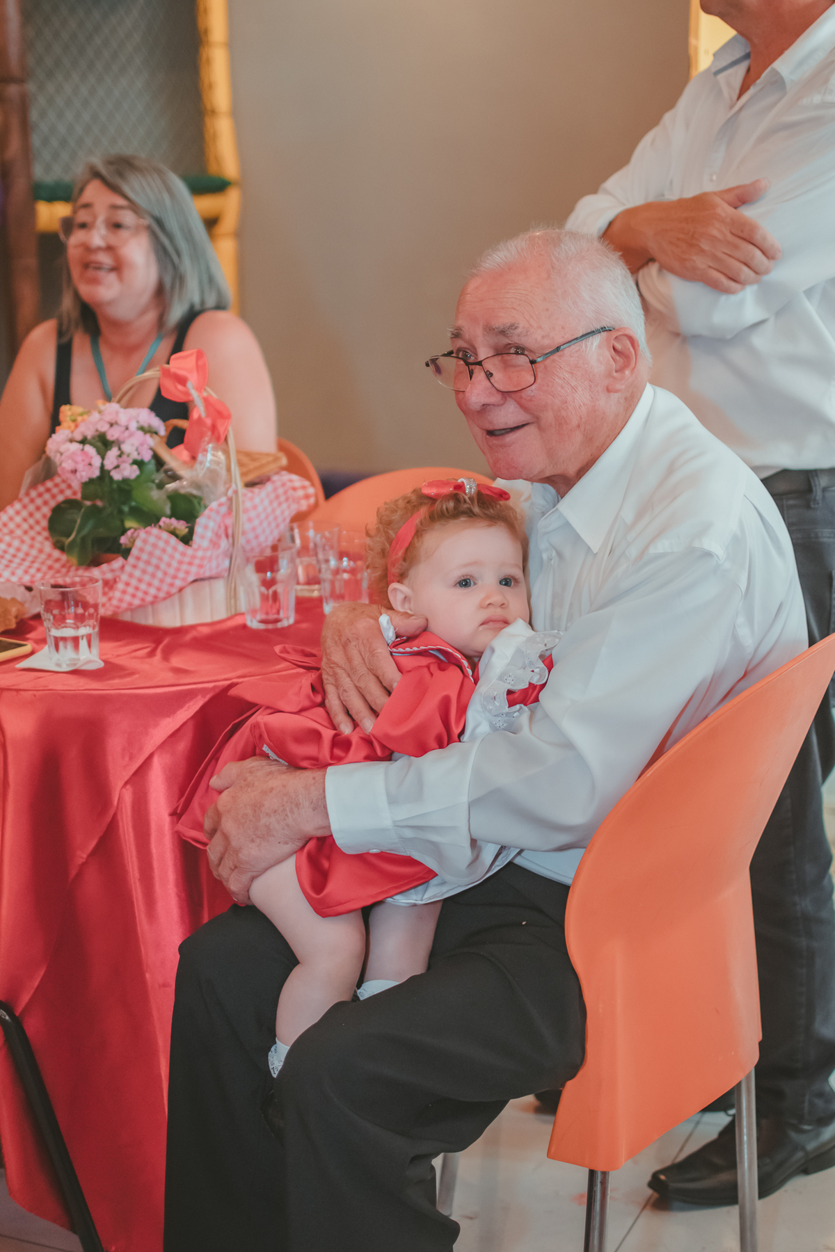 Uma bebê, aconchegada no colo do seu avó, durante a sua festa de aniversário de 1 ano.