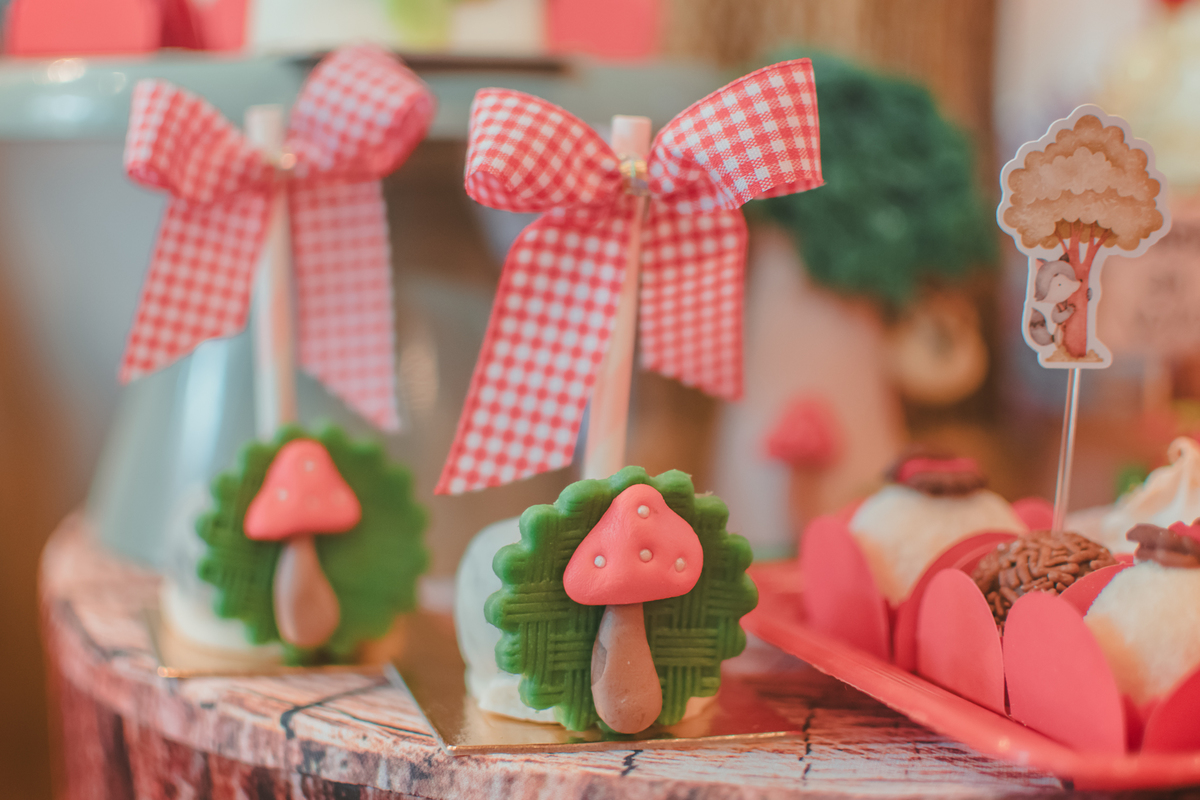 doce de festa infantil com um cogumelo decorativo e uma laço de fitas xadrez nas cores vermelho e branco.
