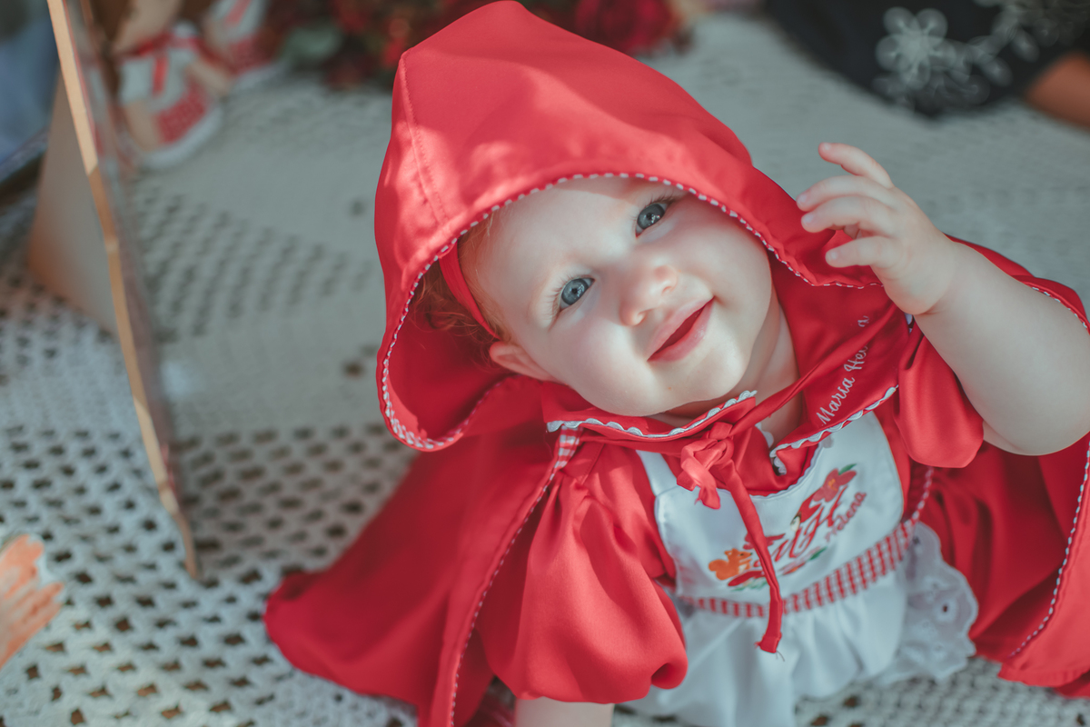 uma bebê de 1 ano usando uma capa Vermelha e brincando em sua festa de aniversário.