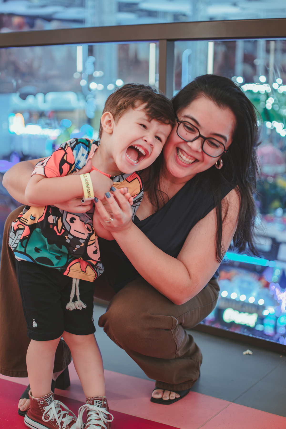 Um menino com sua mãe fazendo cosquinhas e os dois sorrindo abraçados, durante uma festa de aniversário.