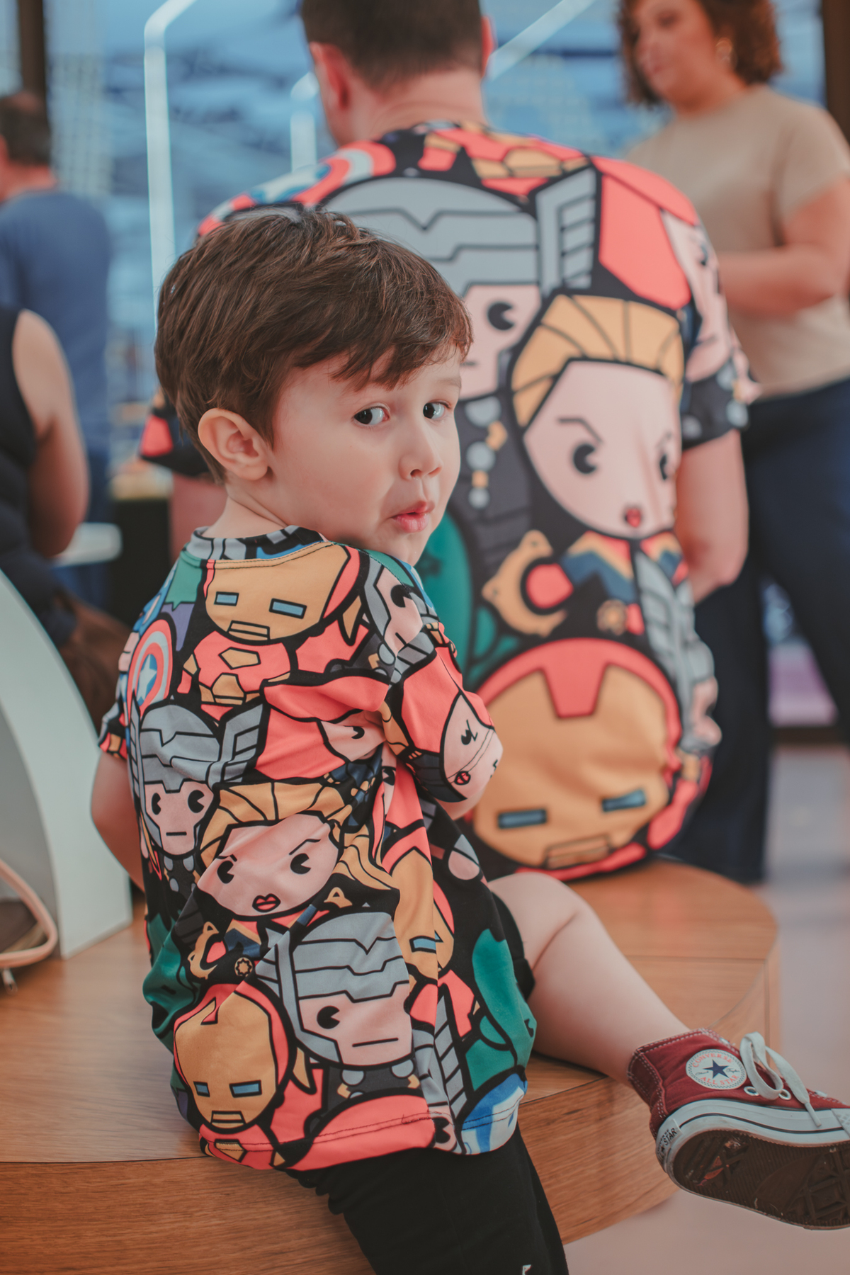 Um menino olhando de costas para a camera, brincando de esconder algum objeto, durante sua festa de aniversário.