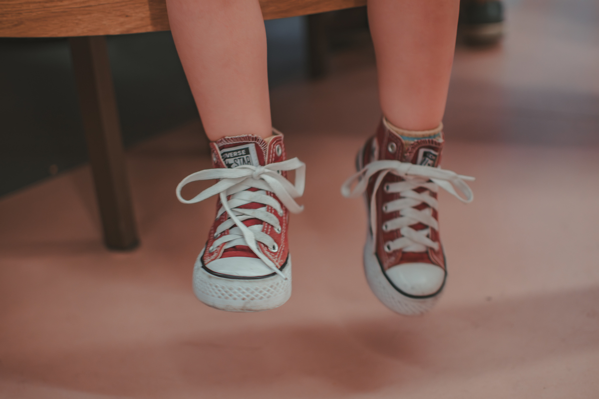 Pés de uma criança calçados com um tenis da marca All star.