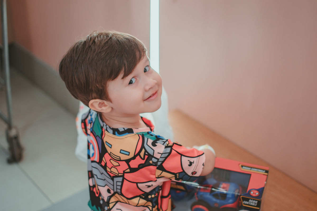 Um menino olhando e sorrindo enquando abre um brinquedo na sua festa de aniversário.