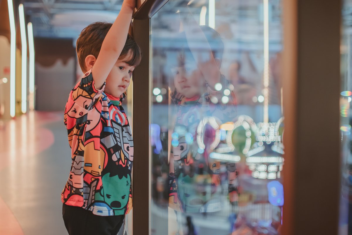 criança perto de uma estrutura de vidro olhando para os brinquedos do parque da sua festa de aniversário.