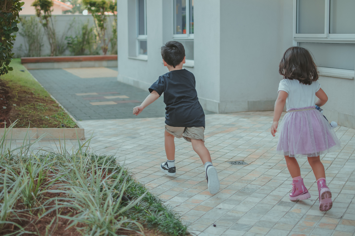 Um menino de camiseta preta correndo ao lado de uma menina de saia e camiseta branca.