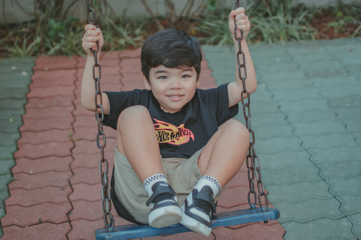 um menino de camiseta preta, brincando no balanço durante uma festa de aniversário infantil.