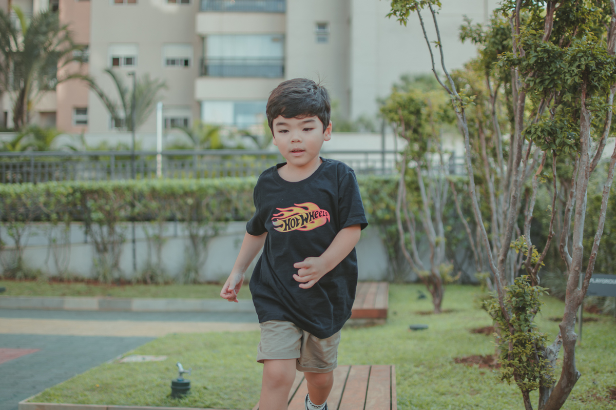 um menino de camiseta preta, brincando de correr sob um banco de madeira, durante uma festa de aniversário infantil.