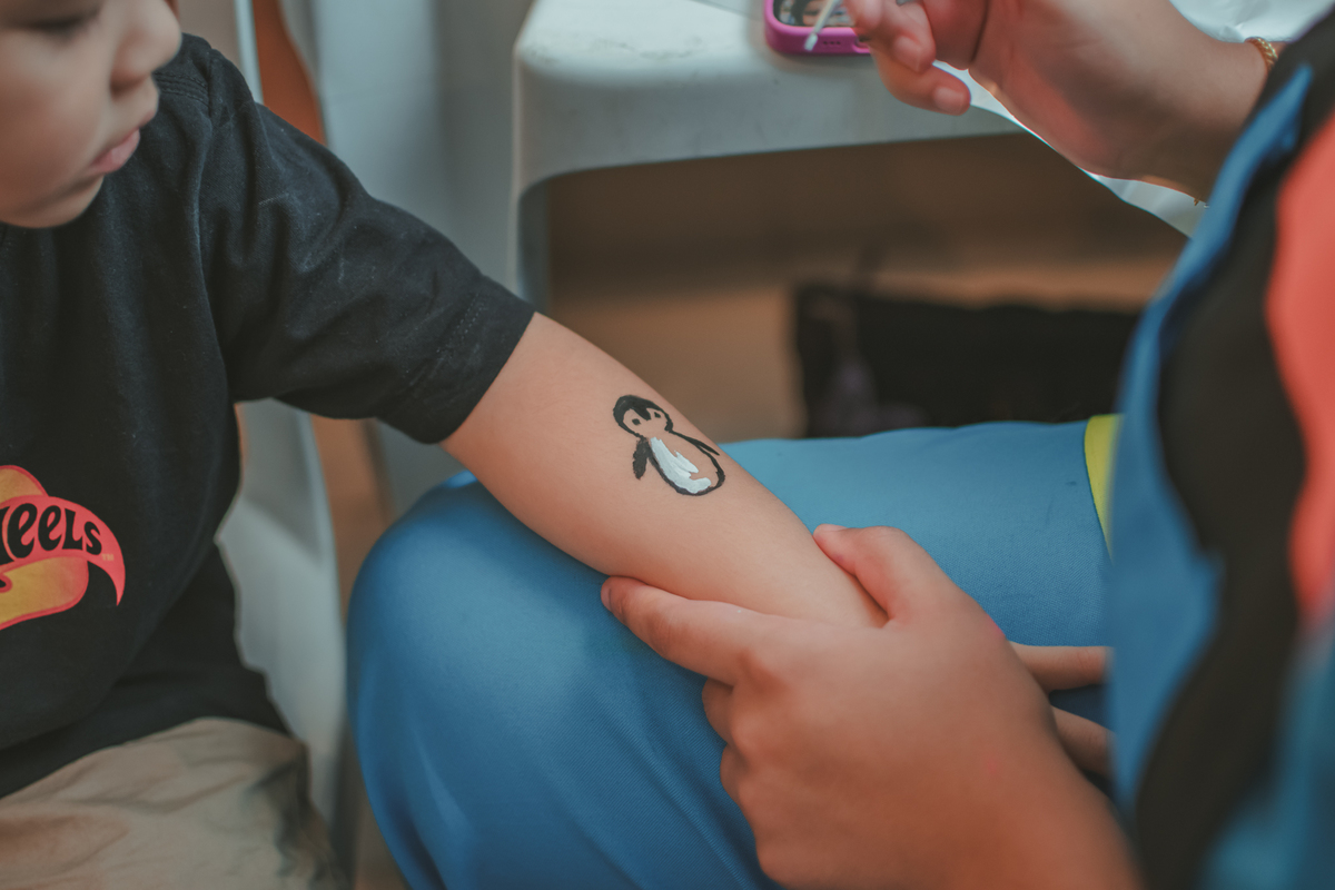 Um menino de camiseta preta, pintando o desenho de um pinguim no branço, durante sua festa de aniverrsário de 4 anos.