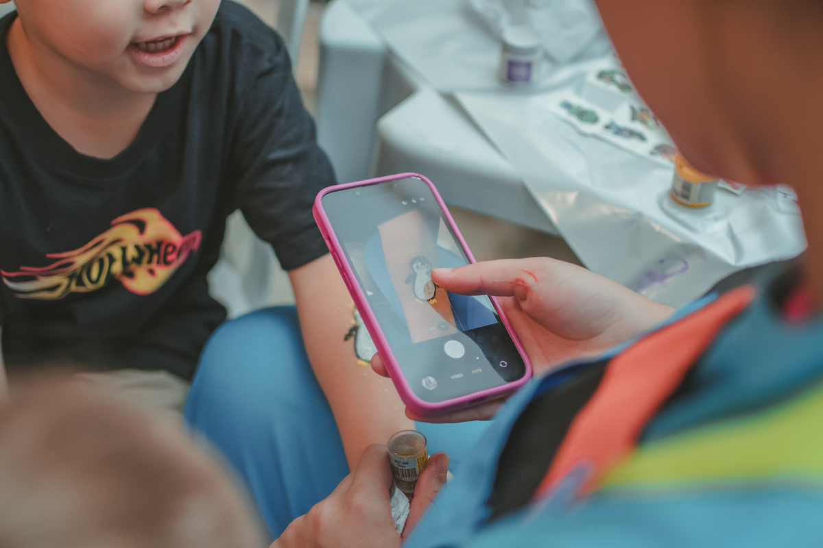 Um menino de camiseta preta, pintando o desenho de um pinguim no branço, durante sua festa de aniverrsário de 4 anos.