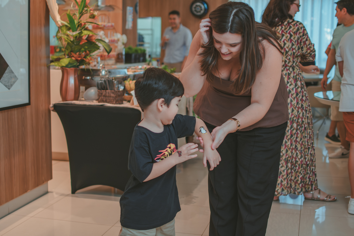 Um menino de camiseta preta, mostrando o desenho de um pinguim no branço para sua mãe, durante sua festa de aniverrsário de 4 anos.