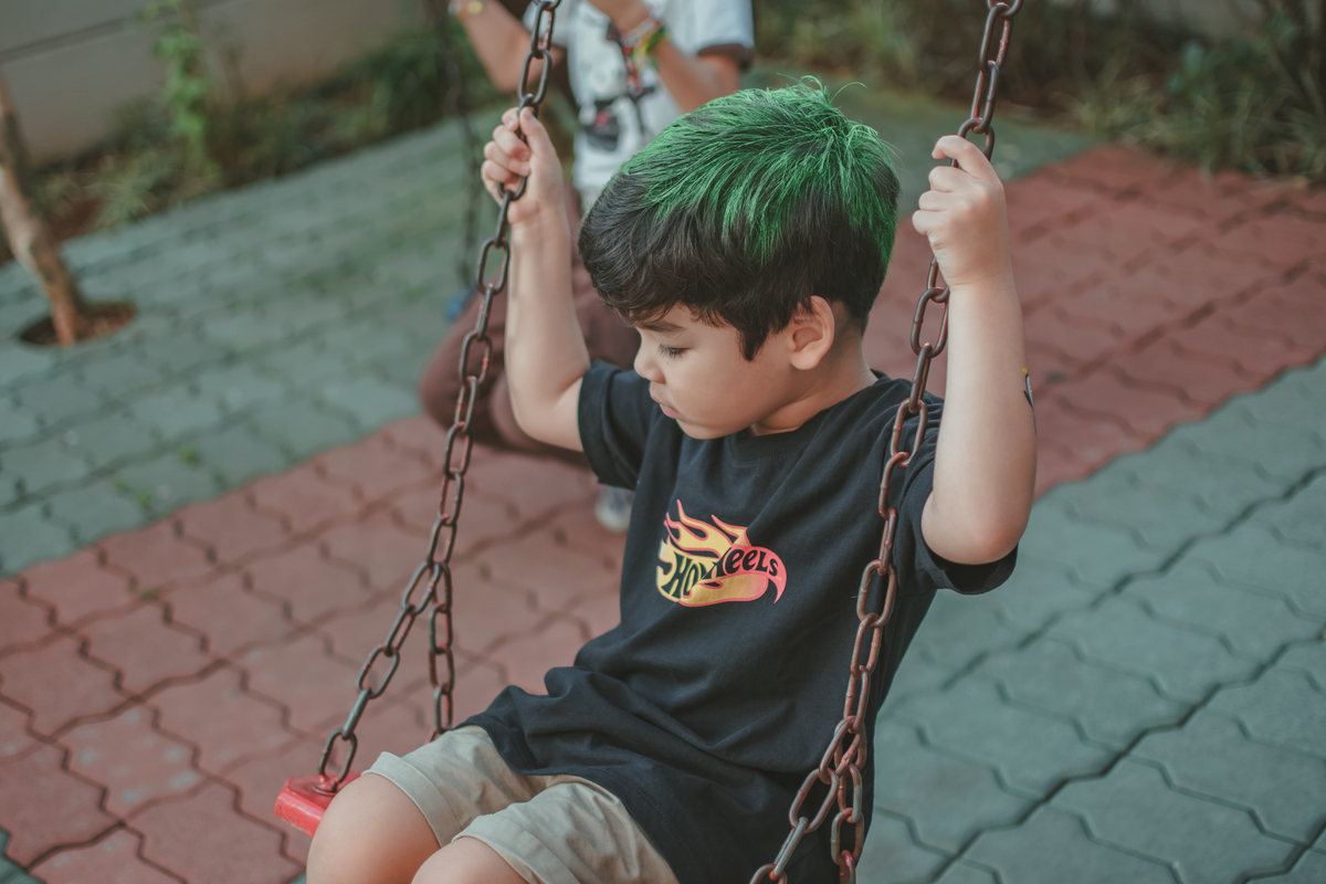 um menino de camiseta preta, brincando no balanço durante uma festa de aniversário infantil.