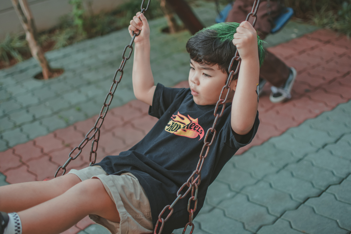 um menino de camiseta preta, brincando no balanço durante uma festa de aniversário infantil.